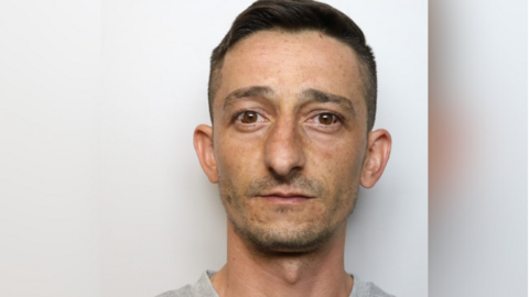 A mug shot of Indogen Erdogan. He has short, dark hair and brown eyes.