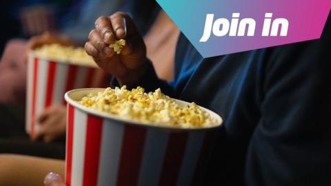 Someone is holding a red and white striped tub of buttery popcorn. They are holding some in their fingertips as if they're about to eat it. 
