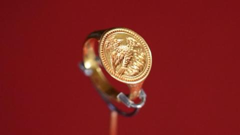 A close-up of a gold ring with a phoenix and flames engraved on it
