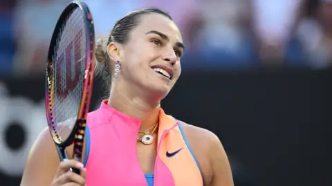 Aryna Sabalenka smiles while holding her racquet