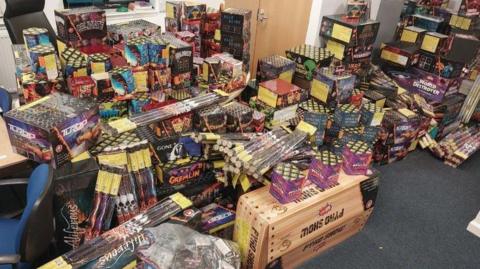 Dozens of boxes of fireworks piled high in an office. 