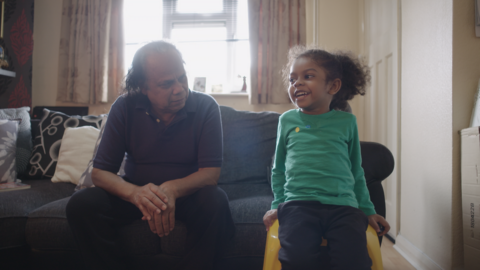 A grandfather and granddaughter talk in the living room.