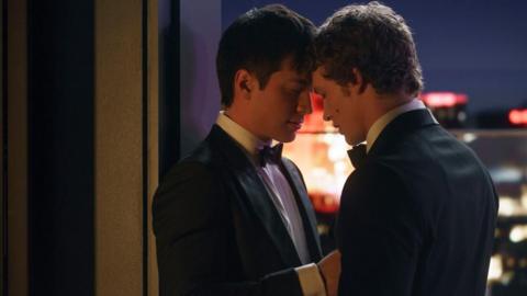 Shane Hollander, played by Hudson Williams, and Ilya Rozanov, played by Connor Storrie, both wearing tuxedos, embrace on a rooftop in a scene from Heated Rivalry. 