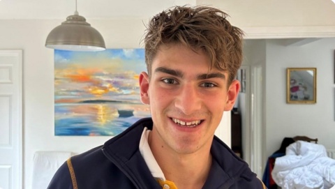 Tom Dunlop is smiling at the camera. He has brown eyes and hair, is wearing a navy sweatshirt.