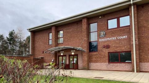 Peterlee Magistrates' Court is a two storey red brick building. There is a crest on the front of the building and a white sign that says: "MAGISTRATES' COURT".