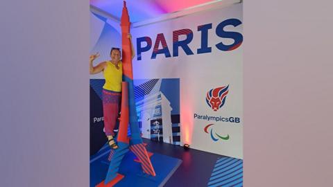 Image shows Kim Brinkworth climbing a model of the Eiffel Tower with the Paralympics GB logo in the background