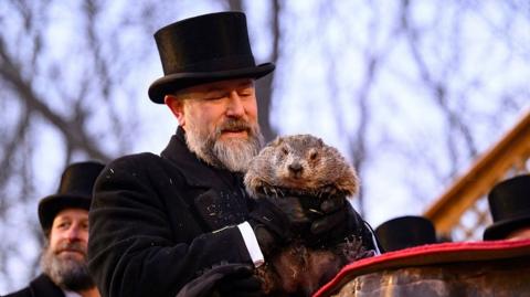 Groundhog handler AJ Dereume, wearing a black top hat and black coat, holds Punxsutawney Phil