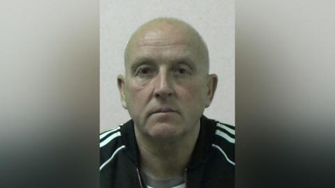 Mugshot of Michael Stewart. He is bald and clean shaven and is wearing a black Adidas jacket with white stripes on the sleeves.