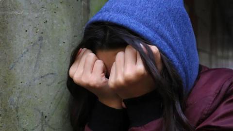 Unidentifiable young person wearing a blue hood with head in hands