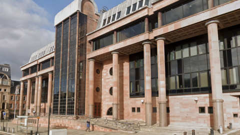 The outer exterior of Newcastle Magistrates Court, a grand building with columns lining the outside with black tinted windows.