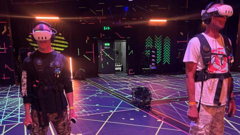 Two men in virtual reality headsets and jackets on a dancefloor