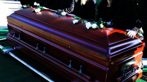 A wooden adult coffin with white roses placed across the top