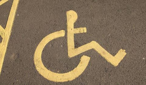 A disabled parking bay on tarmac. There is a yellow disabled parking sign on the ground. 