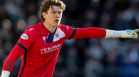 Jon McCracken, wearing a red goalkeeper's jersey, points during a game for Dundee in the 2025-26 season