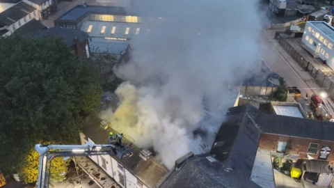 Drone shot of white smoke spilling out from the roof of a building 