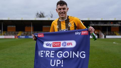 Cambridge United's Paul Digby holds the 'We're Going Up' flag after the club won promotion to League One in 2021