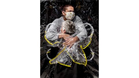 An 85-year-old Brazilian woman is embraced by a nurse at a care home through a transparent hug curtain