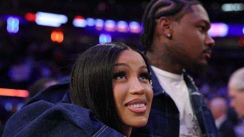 Rapper Cardi B with her boyfriend Stefon Diggs who has his arm around her. Stefon is on the right and in the background looking ahead while Cardi B is in the centre of the picture looking towards the sky