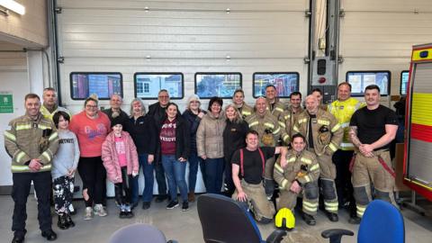 A group of actors and firefighters - actors in plain clothes and firefighters in uniform.