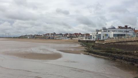 Bridlington beach and seafront with the Spa building on the right hand side and buildings curving to the left of the frame 