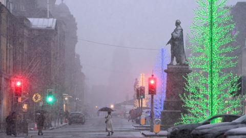 George Street in Edinburgh in heavy snow. The lights from the christmas trees can be seen through heavy snow and people are crossing the road