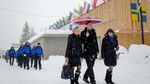 People walk through the town of Davos as snow falls ahead of the World Economic Forum