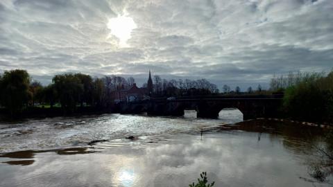 A view of a bridge Warrington, with the sun shining through the cloudy sky and reflecting on the river