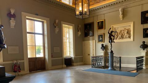 A grand hall with paintings and busts on the walls and a sculpture in the middle.