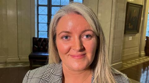 A blonde woman wearing a grey chequered jacket 