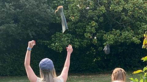A woman wearing a blue hat throws a wellington