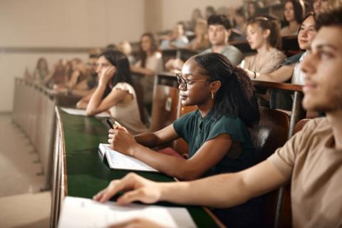 Students, including a young woman and a young man in the foreground, sit in a lecture hall.