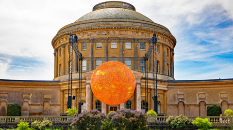 The Helios sculpture on display at Ickworth House. It is a large sphere shape and has been lit up in a yellow colour.