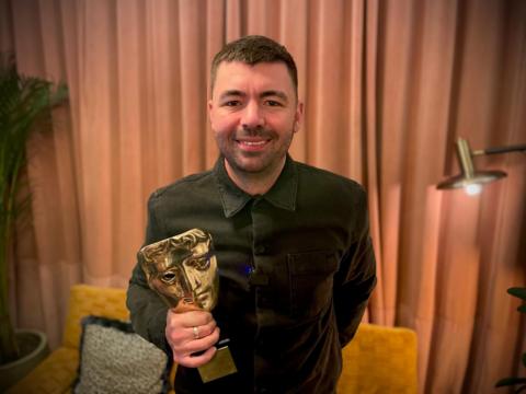 Man in black shirt holding gold Bafta award