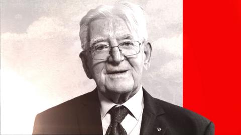 A black-and-white photo of an elderly man looking into the camera. He has white hair and square glasses. He is wearing a black suit and tie. The photo is laid on top of a speckled grey-ish background, with a solid red bar running down the right-side of the screen.