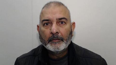 A mugshot of Mohammed Zahid looking at the camera while wearing a dark jumper, he has a grey beard and short hair.