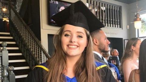 Grace Millane pictured in front of a grand staircase at her university graduation. She is smiling.