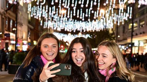 Three girls take a photo of themselves by Oxford Street lights