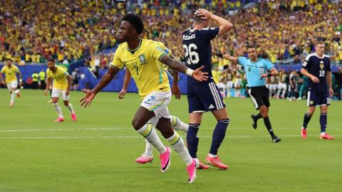 MIAMI, FLORIDA - JUNE 24: Vinicius Junior of Brazil celebrates scoring the opening goal in front a dejected Scott McKenna of Scotland during the FIFA World Cup 2026 Group C match between Scotland and Brazil at Miami Stadium on June 24, 2026 in Miami, United States. (Photo by Marc Atkins/Getty Images)