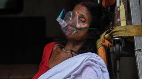 An elderly woman with breathing difficulty inhales medication with the help of nebuliser or oxygen mask, inside an ambulance, at MMCH hospital in Guwahati, Assam, India on 25 May 2021.