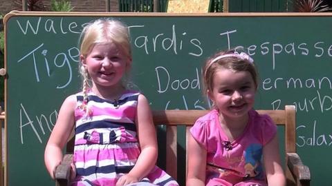 Two girls sat on benches in front of a blackboard