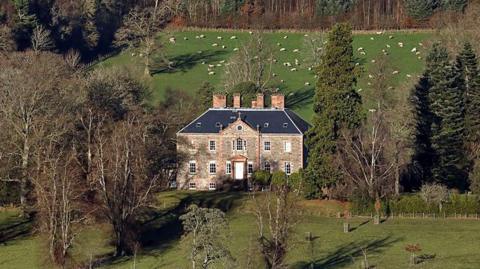 Torwoodlee House in the Borders - an impressive brick building with a number of chimneys nestled between trees with farmland around
