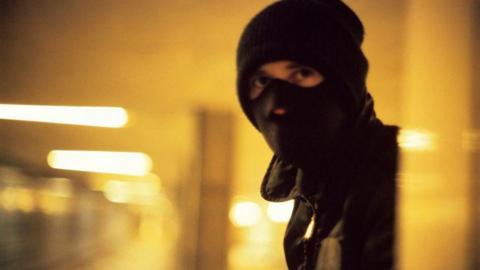 A masked man who is laying wait wearing a balaclava.