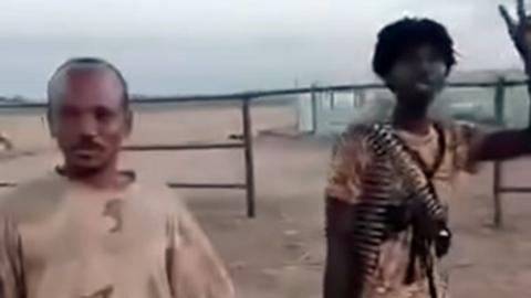 A screengrab of two RSF fighters in el-Fasher's cattle market - one with a belt of ammunition around his neck holds up a victory sign