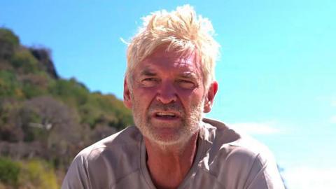 Headshot of Phillip Schofield with a beard and dishevelled hair squinting in the sun while on a beach in Madagascar, a promo image for the new Cast Away show on Channel 5