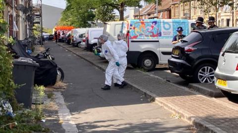 Police officers and forensic officers stand on a residential street.