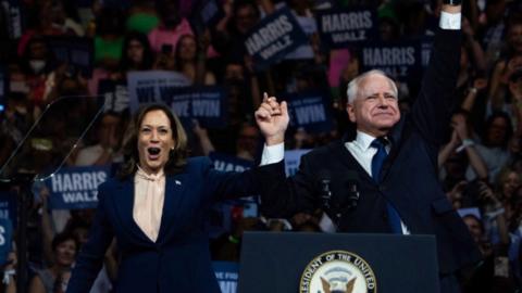 Kamala Harris and Tim Walz hold arms up at rally