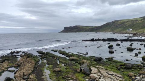 Grey clouds over a rugged coastline and calm sea.