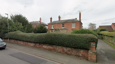 A two storey Georgian-style house pictured from the street with a large hedge covering the view of the bottom floor. 