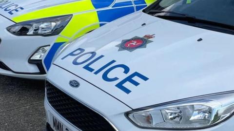 A close up of two police cars parked next to each other. They are white with yellow and blue branding. On the bonnets the word is the word police in capital letters and the Isle of Man Constabulary badge.