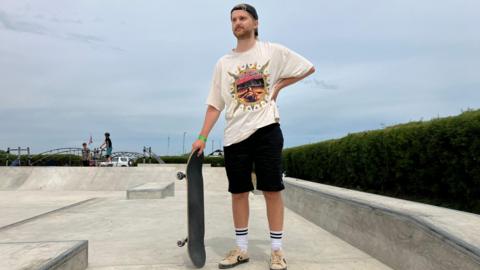 Skateboarder wearing cap and shorts stands on the new concrete surface of the skatepark